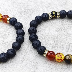 Peut inclure: Deux bracelets extensibles composés de perles en pierre de lave noire poreuse et d'une série de sept perles chakra lisses et multicolores. Chaque bracelet comprend des entretoises en métal doré avec des strass et une perle noire avec du texte doré.