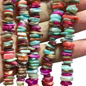 Könnte beinhalten: Eine mehrsträngige Halskette mit kleinen, unregelmäßigen, polierten Muschelperlen in einer leuchtenden Farbpalette aus leuchtendem Pink, Türkis, Koralle, Weiß und Braun. Die Perlen sind in mehreren vertikalen Reihen aufgereiht.