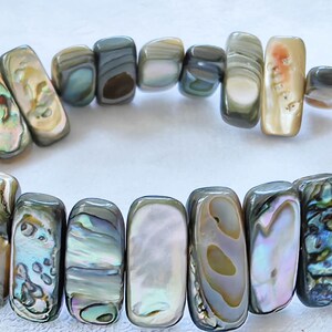 Puede incluir: Una pulsera compuesta por cuentas rectangulares de concha pulida con tonos iridiscentes de verde, azul, rosa y crema. Las cuentas están dispuestas en un bucle continuo, mostrando variaciones naturales en color, brillo y textura en cada pieza.
