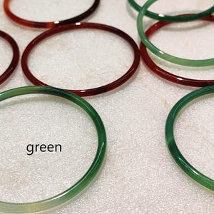 May include: A collection of thin, circular bangles in shades of red and green. The bangles are arranged in a group, with some overlapping. The text red is positioned near the red bangles, and the text green is positioned near the green bangles.