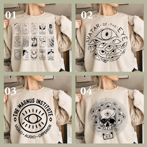 Op de afbeelding: Vier beige sweatshirts met zwarte grafische ontwerpen. De ontwerpen omvatten tarotkaarten, meerdere ogen met de tekst "AVATAR OF THE EYE", de tekst "THE MAGNUS INSTITUTE VIGILO AUDIO OPPERIOR" en een schedel met ogen en een cassette.