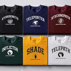 Puede incluir: Seis camisetas de varios colores, cada una con una palabra &uacute;nica en una fuente universitaria: Hydrokinetic, Teleporter, Htechnopath, Inflictor, Shade y Telepath. Cada camiseta tambi&eacute;n tiene el texto "Keepers of the Lost Cities".