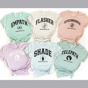 Puede incluir: Seis camisetas de manga corta en varios colores pastel, cada una con una palabra diferente en una fuente universitaria: Empath, Flasher, Htechnopath, Inflictor, Shade y Telepath. Cada camiseta tambi&eacute;n tiene un peque&ntilde;o gr&aacute;fico y el texto "Keepers of the Lost Cities."