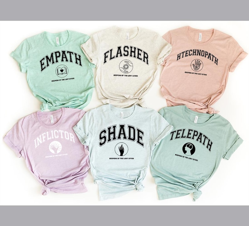 Puede incluir: Seis camisetas de manga corta en varios colores pastel, cada una con una palabra diferente en una fuente universitaria: Empath, Flasher, Htechnopath, Inflictor, Shade y Telepath. Cada camiseta tambi&eacute;n tiene un peque&ntilde;o gr&aacute;fico y el texto "Keepers of the Lost Cities."