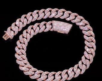 May include: A rose gold chain necklace with a cuban link design. The necklace is encrusted with numerous small, clear gemstones. The clasp is rectangular and also covered in gemstones. The background is black.