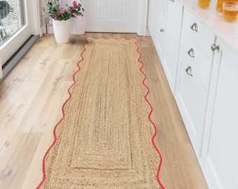 Puede incluir: Una alfombra de pasillo rectangular de yute con un borde rojo festoneado. La alfombra está hecha de fibras naturales tejidas y está colocada sobre un suelo de madera clara. El diseño de la alfombra presenta un patrón rectangular central.