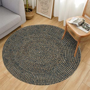 以下が含まれることがあります： 同心円デザインの丸いラグ。濃い青とタン色の配色で、織り込まれた質感があります。木製の床に置かれ、ソファや椅子などの家具に囲まれています。