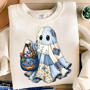 Pode incluir: Uma camisola de gola redonda cor de creme com um gráfico de um fantasma feito de tecido patchwork azul e branco. O fantasma segura um balde de abóbora azul cheio de doces coloridos. O design inclui remendos florais e azuis sólidos.