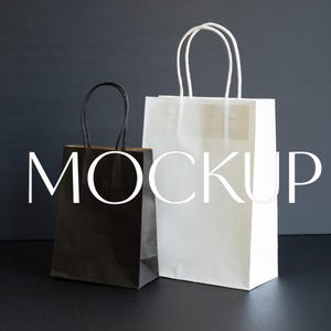 May include: Two paper shopping bags, one black and one white, with twisted paper handles. The word "MOCKUP" is overlaid on the bags in a white, sans-serif font. The bags are on a dark surface.