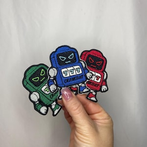 May include: Three embroidered patches in green, blue, and red, each featuring a robot-like design with a slot machine face. The blue patch displays the text "CRANKDAT" and the number "777". The red and green patches also have the number "7".