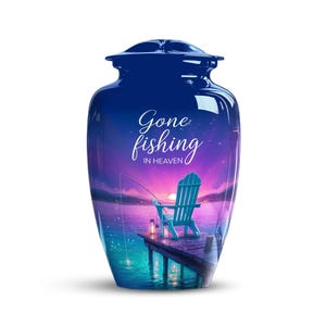May include: A navy blue cremation urn with a scenic lakeside design. The urn features the words "Gone fishing in Heaven" in script. The image depicts a wooden dock, a blue chair, and a fishing rod against a sunset backdrop.
