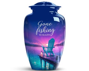 May include: A navy blue cremation urn with a scenic lakeside design. The urn features the words "Gone fishing in Heaven" in script. The image depicts a wooden dock, a blue chair, and a fishing rod against a sunset backdrop.