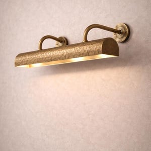 Side-angle view of solid brass picture light, curved arms and round backplate, hand hammered texture