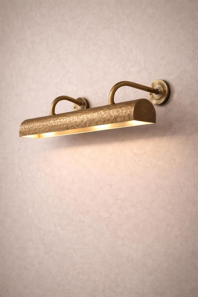 Side-angle view of solid brass picture light, curved arms and round backplate, hand hammered texture