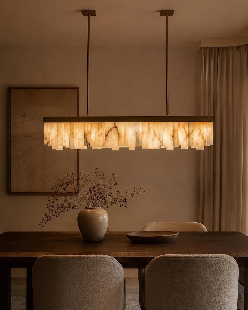 Brass alabaster linear pendant over a dining table; warm, veined alabaster blocks glow softly, an uplight island chandelier.