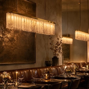 Brass alabaster linear pendant chandelier above a leather dining banquette, casting warm uplight along a row.
