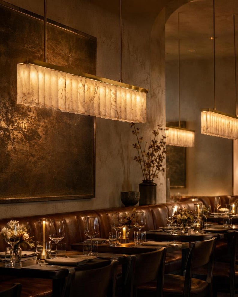 Brass alabaster linear pendant chandelier above a leather dining banquette, casting warm uplight along a row.