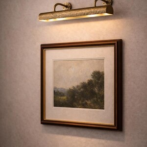 Mid-shot solid brass picture light above framed landscape, slim gallery light, antique brass sheen