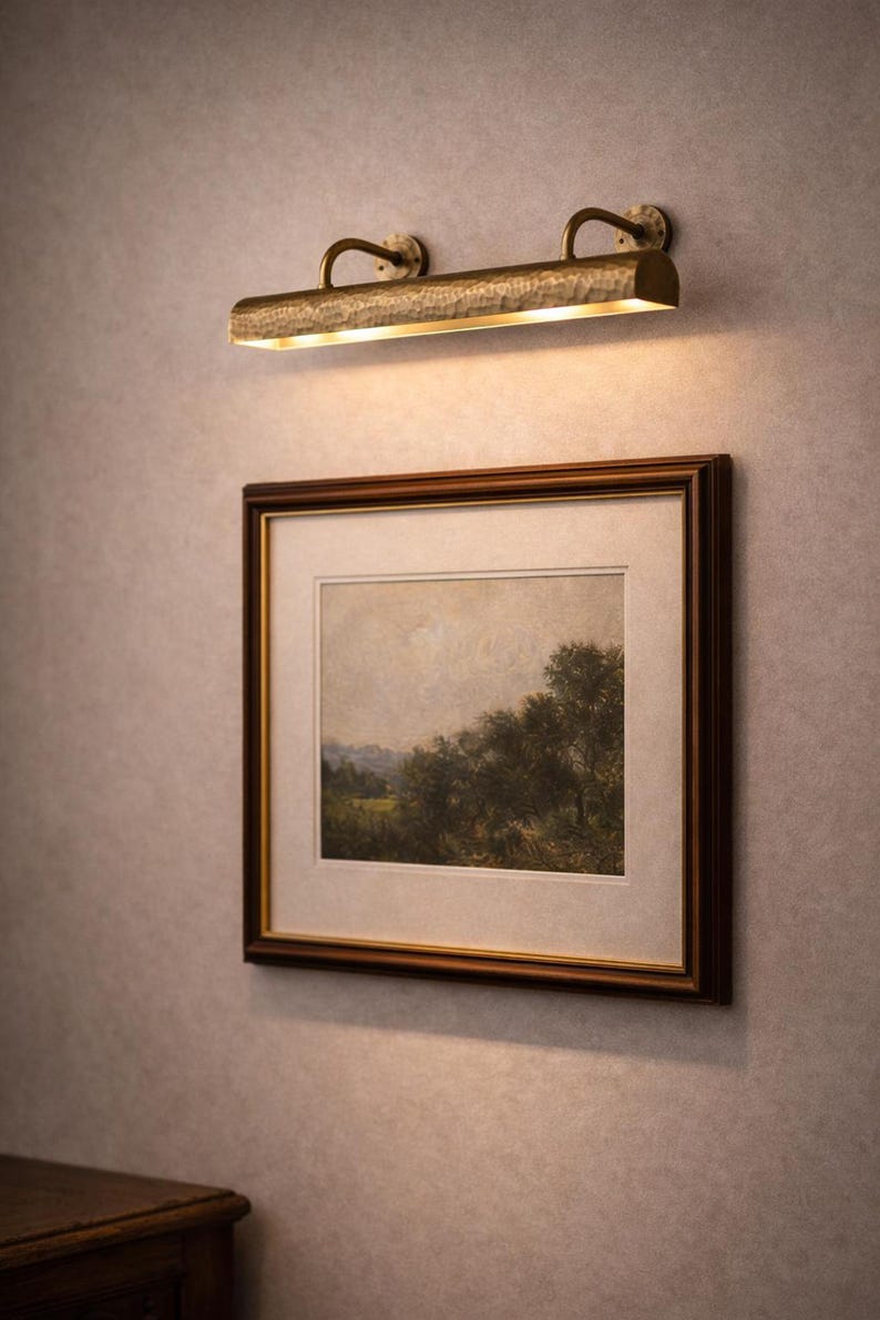 Mid-shot solid brass picture light above framed landscape, slim gallery light, antique brass sheen