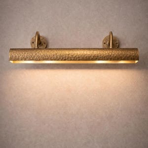 Centered solid brass picture light, hand-hammered finish, soft wash on wall, gallery mood