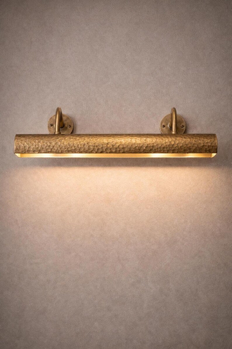 Centered solid brass picture light, hand-hammered finish, soft wash on wall, gallery mood