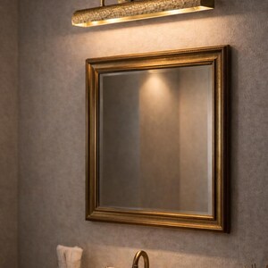 solid brass picture light above a gilded bathroom mirror, mirror picture light, warm luxury finish
