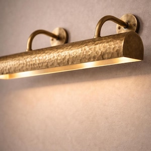 Close-up of hammered bar detail on solid brass picture light, warm downward wash, luxe texture