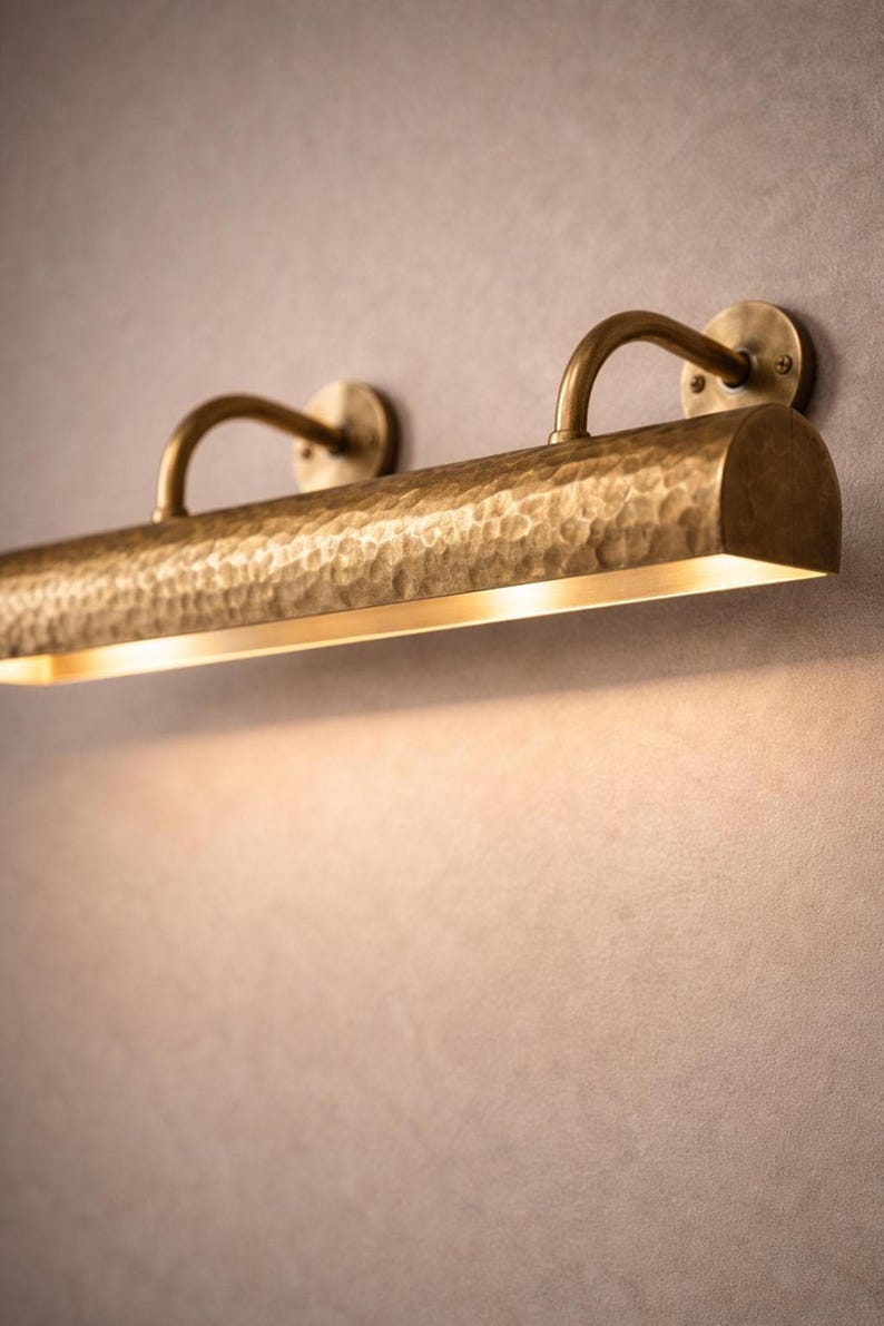 Close-up of hammered bar detail on solid brass picture light, warm downward wash, luxe texture
