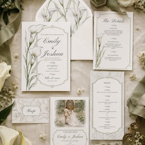 May include: A wedding stationery set featuring white paper with green calla lily illustrations. Includes an invitation, a details card, a menu, an RSVP card, and a save the date card with a photo of a couple. An envelope with a floral liner and a gold ring in a green velvet box are included.