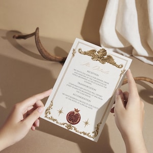 K&ouml;nnte beinhalten: Einladungskarte mit aufwendigen goldenen Details und Text. Die Karte zeigt eine Engel-Illustration oben und eine Granatapfel-Grafik unten. Der Text lautet "The Details" und enth&auml;lt Informationen &uuml;ber Empfang, Transport und Unterkunft.