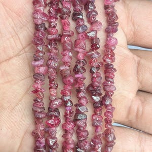 May include: Strands of raw, uncut, pink and red tourmaline gemstone beads. The beads are irregular in shape and size, strung together to create a necklace or bracelet. The gemstones have a natural, unpolished appearance.