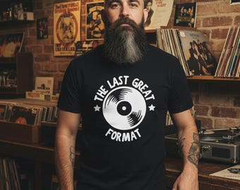 May include: Black t-shirt with the text "THE LAST GREAT FORMAT" and a graphic of a vinyl record. The man in the image is standing in a room with vinyl records and posters on the brick wall.