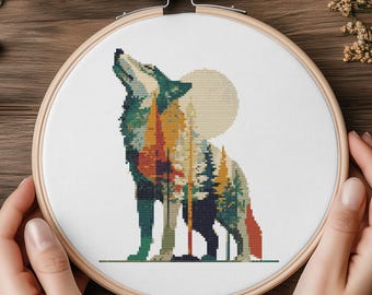 May include: A cross-stitch embroidery hoop showing a howling wolf silhouette against a forest and moon backdrop. The wolf is in green, orange, and brown. The design is set within a wooden embroidery hoop.