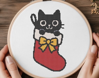 May include: A cross-stitch embroidery hoop featuring a black cat peeking out of a red Christmas stocking with a yellow bow. The cat has white eyes and a white chest. The embroidery is set against a white fabric.