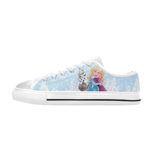 May include: White canvas low-top sneakers with a light blue background featuring a winter scene with cartoon characters. The design includes Elsa, Anna, and Olaf. The shoes have white laces and a black stripe on the sole.