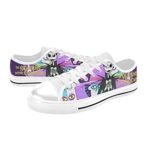 May include: White canvas low-top sneakers featuring a colorful design from "The Nightmare Before Christmas." The shoes have a white toe cap, white laces, and a black stripe along the sole. The design includes Jack Skellington and other characters.