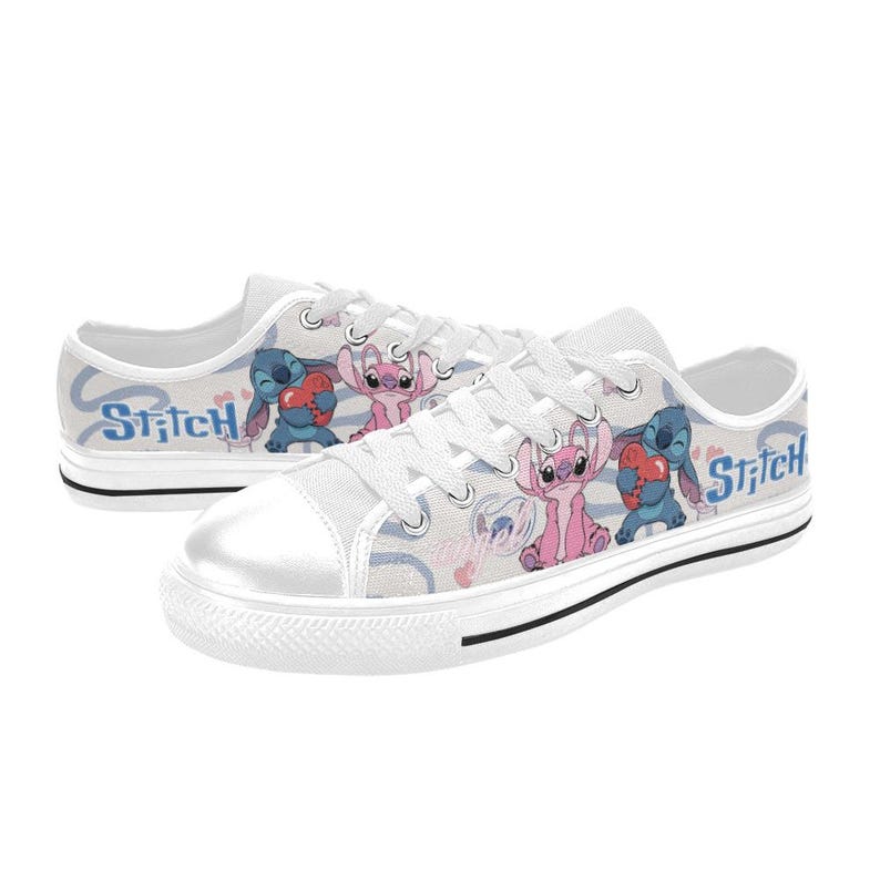 Pu&ograve; includere: Scarpe da ginnastica in tela bianca con un design a cartoni animati di Stitch e Angel. Le scarpe hanno una suola in gomma bianca, lacci bianchi e la parola "Stitch" in blu sul lato. Il design include cuori e uno sfondo azzurro.