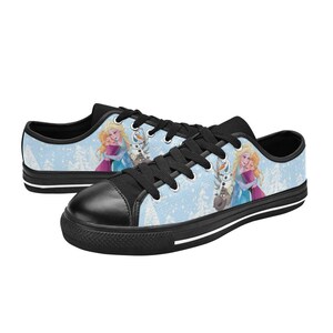 May include: Pair of low-top canvas sneakers featuring a light blue background with a winter scene and characters. The shoes have black laces, toe caps, and soles. The design includes images of two princesses and a snowman.