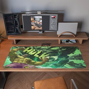 Könnte beinhalten: Rechteckige Schreibtischunterlage mit Hulk im Comic-Stil. Hulk wird in einer dynamischen Pose mit grüner Haut, lila Shorts und dem Wort "HULK" in großen grünen Buchstaben dargestellt. Der Hintergrund hat grüne und weiße Blitze.