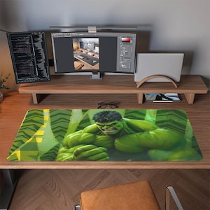 Könnte beinhalten: Ein grünes und gelbes Hulk-Mauspad mit einer detaillierten Illustration von Hulk. Das Mauspad ist rechteckig und liegt auf einem Holzschreibtisch, mit Computermonitoren und einem Laptop-Ständer im Hintergrund.