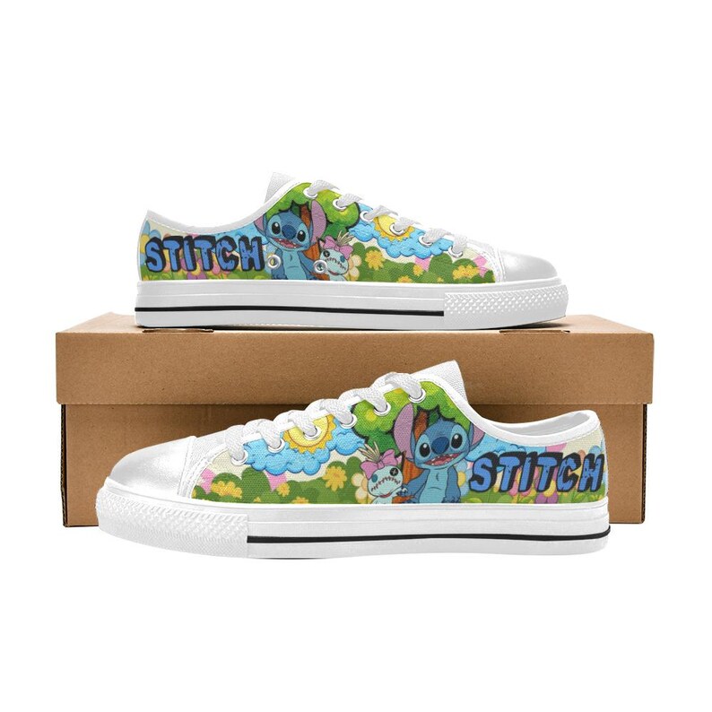 May include: White canvas trainers with a colourful design featuring the character Stitch and the word "Stitch" in blue. The shoes have a white rubber sole and are displayed on a cardboard box.