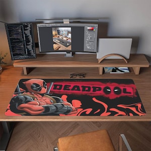 May include: A rectangular desk mat featuring the Deadpool character in red and black. The mat has the word "DEADPOOL" in red block letters with a black background and red flames.