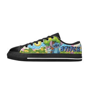May include: Black and white low-top canvas trainers with a colourful graphic of Stitch and Angel from Lilo & Stitch. The design includes the word "Stitch" in blue letters. The trainers have black laces and a black rubber sole.