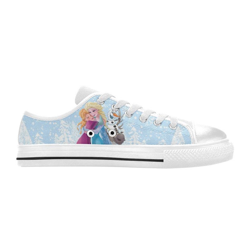 May include: Light blue canvas sneakers featuring a graphic of two characters from the animated movie Frozen, with a winter forest background. The shoes have white laces, a white rubber sole, and a black stripe.