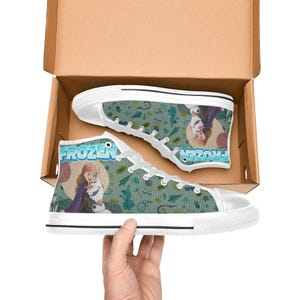 Może przedstawiać: Wysokie trampki pł&oacute;cienne z białą gumową podeszwą i sznurowadłami. Trampki mają turkusowe tło ze wzorem płatk&oacute;w śniegu i postaci z filmu "Frozen". Słowo "FROZEN" jest nadrukowane z boku.