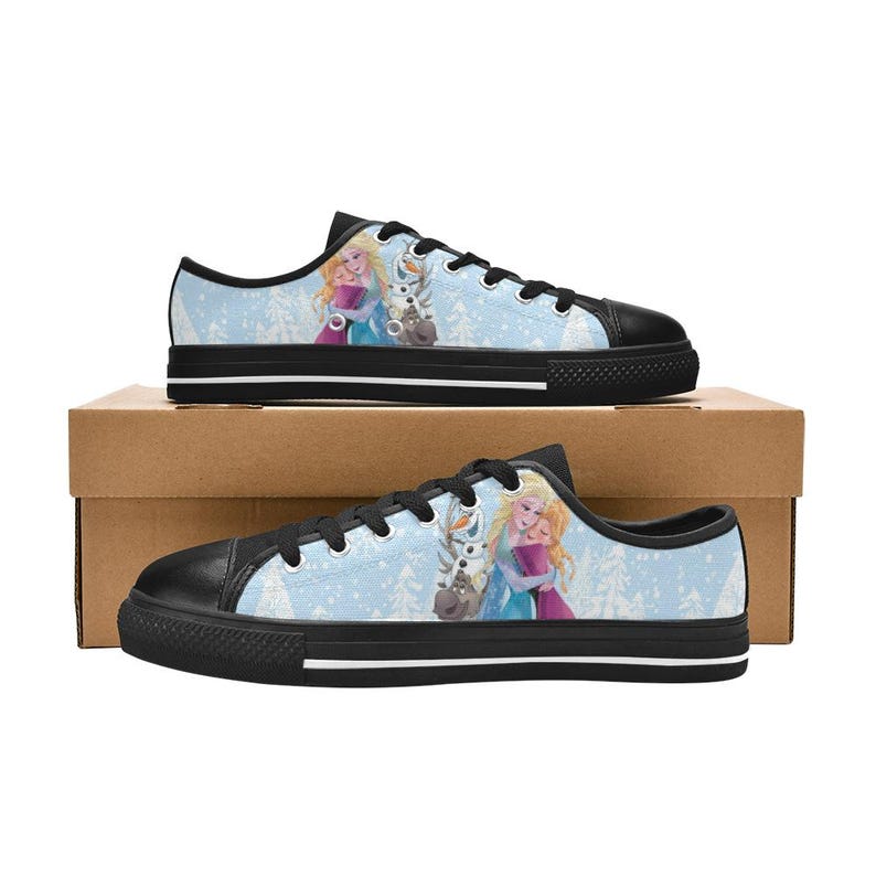 May include: Pair of blue canvas sneakers featuring a winter scene with two characters and a snowman. The shoes have black soles and laces, and are set against a light blue background with a winter forest design.