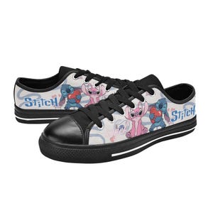 Pu&ograve; includere: Un paio di scarpe da ginnastica basse in tela con i personaggi Stitch e Angel. Le scarpe hanno la punta nera, lacci neri e suola bianca con una striscia nera. Il design include la parola "Stitch" e immagini dei personaggi.