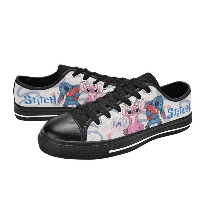 Pu&ograve; includere: Un paio di scarpe da ginnastica basse in tela con i personaggi Stitch e Angel. Le scarpe hanno la punta nera, lacci neri e suola bianca con una striscia nera. Il design include la parola "Stitch" e immagini dei personaggi.