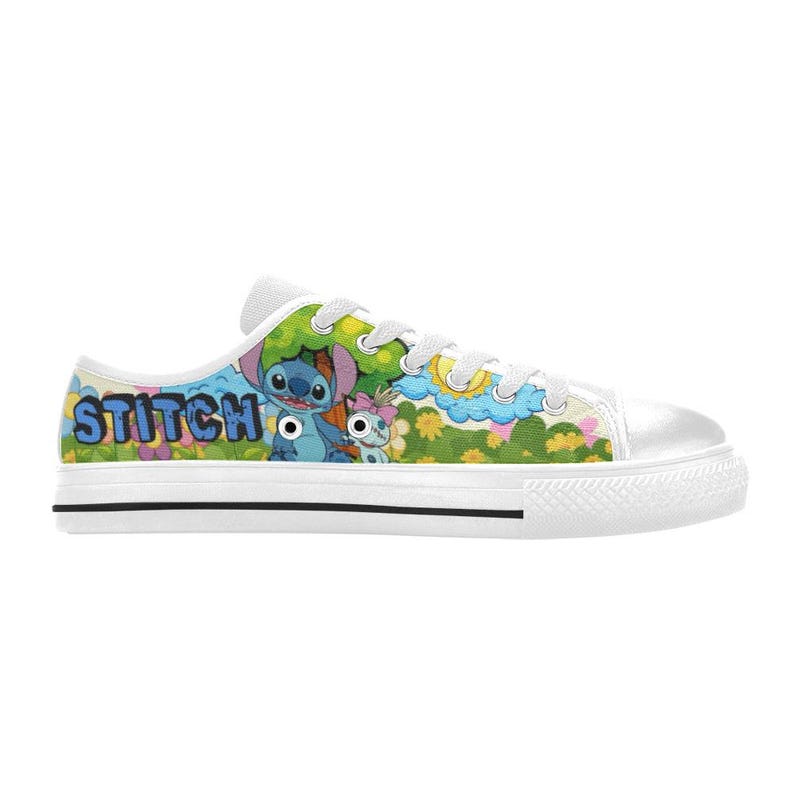 May include: White canvas trainers with a vibrant graphic of Stitch and a friend in a playful outdoor setting. The word "STITCH" is printed in blue. The trainers have white laces and a black stripe on the sole.