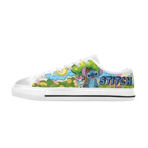 May include: White canvas trainers with a colourful cartoon design featuring Stitch and a friend. The design includes blue, green, yellow, and pink elements, with the word "Stitch" in blue letters. The shoes have a white rubber sole.